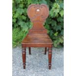 A Victorian mahogany hall chair with a carved & shaped back, hard seat, & on turned tapered legs (