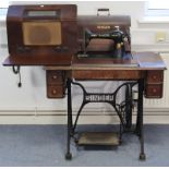 A Singer treadle sewing machine in a walnut case on a cast-iron base, 36” wide; together with a