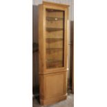 An oak tall narrow corner cabinet with six adjustable plate-glass shelves enclosed by a glazed