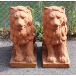 A pair of moulded terracotta garden statues in the form of seated lions, each on rectangular