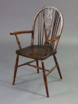 A Windsor-style wheel-back elbow chair with a hard seat, & on turned legs with spindle stretchers.
