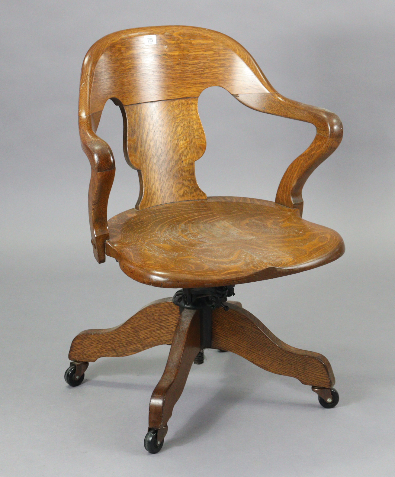 An oak revolving desk chair with a shaped splat back, hard seat & on a sprung base with four splay