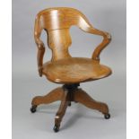 An oak revolving desk chair with a shaped splat back, hard seat & on a sprung base with four splay
