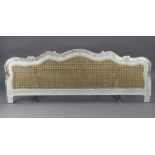 A continental-style white painted & carved wooden footboard inset with a woven-cane panel, 76¼”