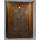 A 19th century oak hanging corner cupboard fitted two shaped shelves enclosed by a carved “floral”