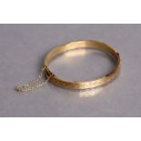 An un-marked yellow metal stiff hinged bangle with engraved decoration (11.8g).
