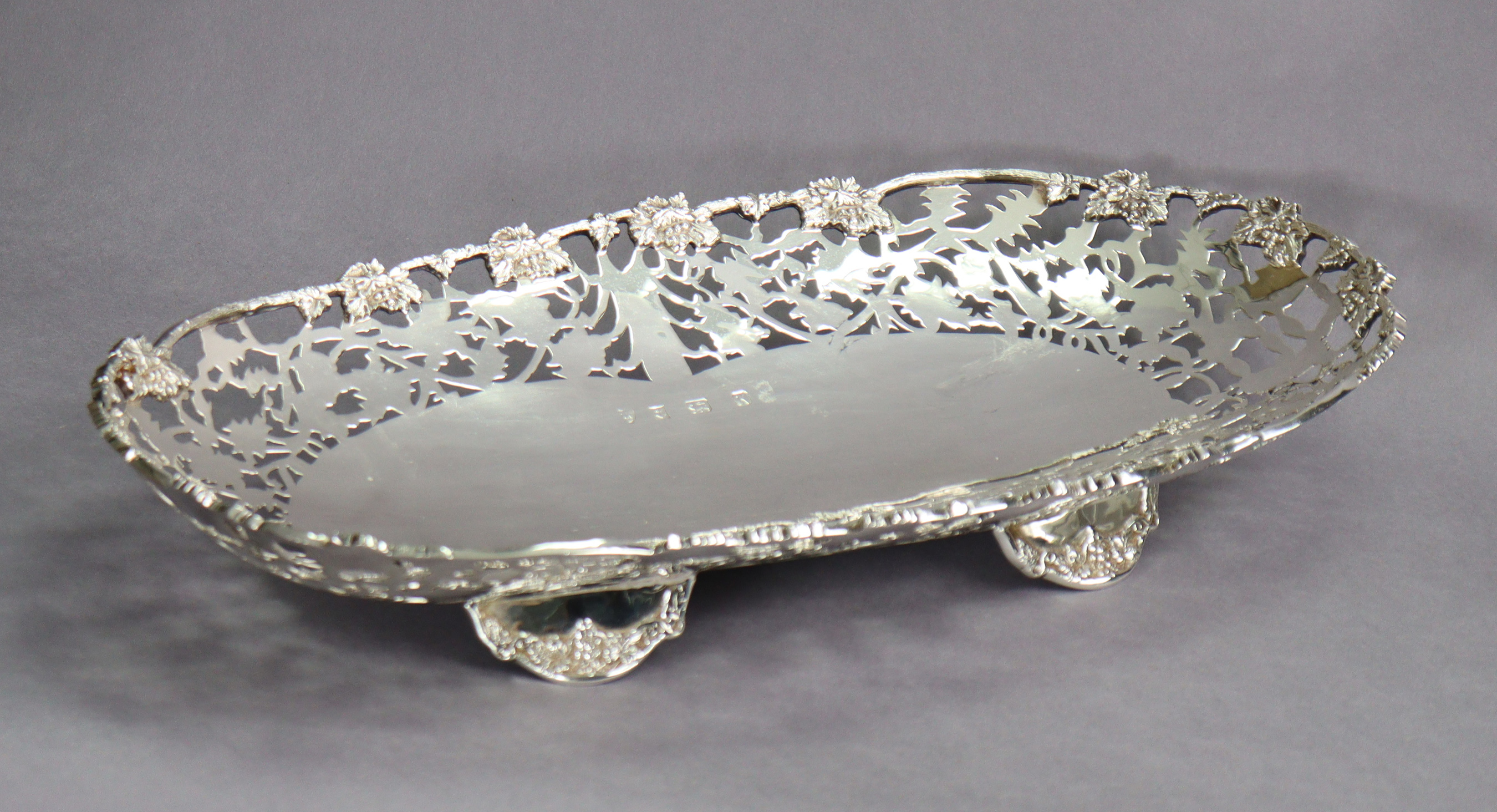 An Elizabeth II silver large oval dish with cast grapevine rim & wide pierced border, on four