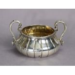 A George V silver sugar bowl of squat round fluted form, with scroll handles & engraved family