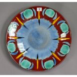 A Poole pottery charger of crimson ground & with multi-coloured geometric design, 15” diameter.