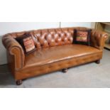 A BUTTONED & BRASS-STUDED TAN LEATHER THREE-SEATER CHESTERFIELD SETTEE with scroll-arms, & on turned