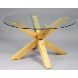 A modern dining table with circular tempered glass top, on a light-oak shaped pedestal base, 55”