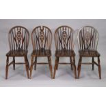 A set of four wheel-back dining chairs with hard seats, & on turned legs with spindle stretchers.