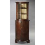 A mahogany small bow-front hanging corner cabinet fitted two shelves enclosed by a glazed door,