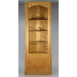 A pine tall standing corner cupboard with three shaped shelves above, with a panel door below, &
