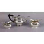 An Edwardian silver three-piece tea service of plain oval form, the teapot on four short foliate