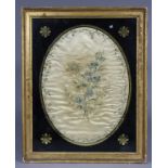An early 19th century coloured silk oval picture of a floral bouquet in a border of entwined