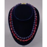 A necklace of opaque ruby oval facetted beads, 20½” long; & another of spherical sapphire beads,