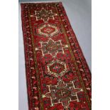 A Persian Heriz runner of madder ground with a row of repeating geometric designs surrounded by