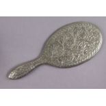 An eastern white metal hand mirror with all-over chased decoration of flowers & foliage, inset