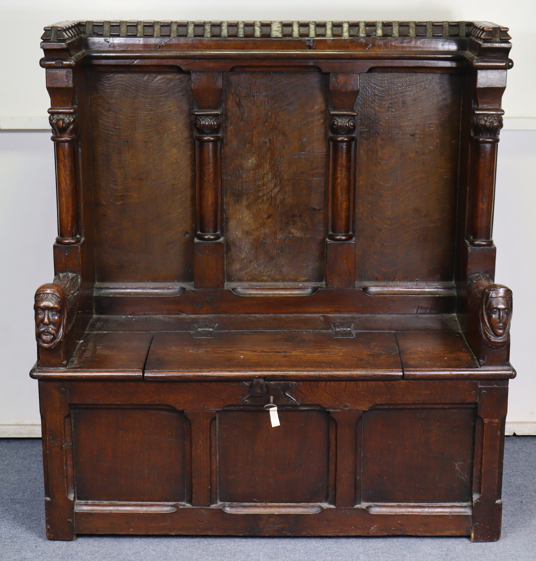 A late Victorian oak box-seat settle in the Gothic manner, the castellated panelled back flanked