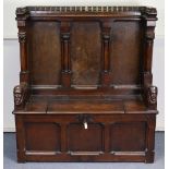 A late Victorian oak box-seat settle in the Gothic manner, the castellated panelled back flanked