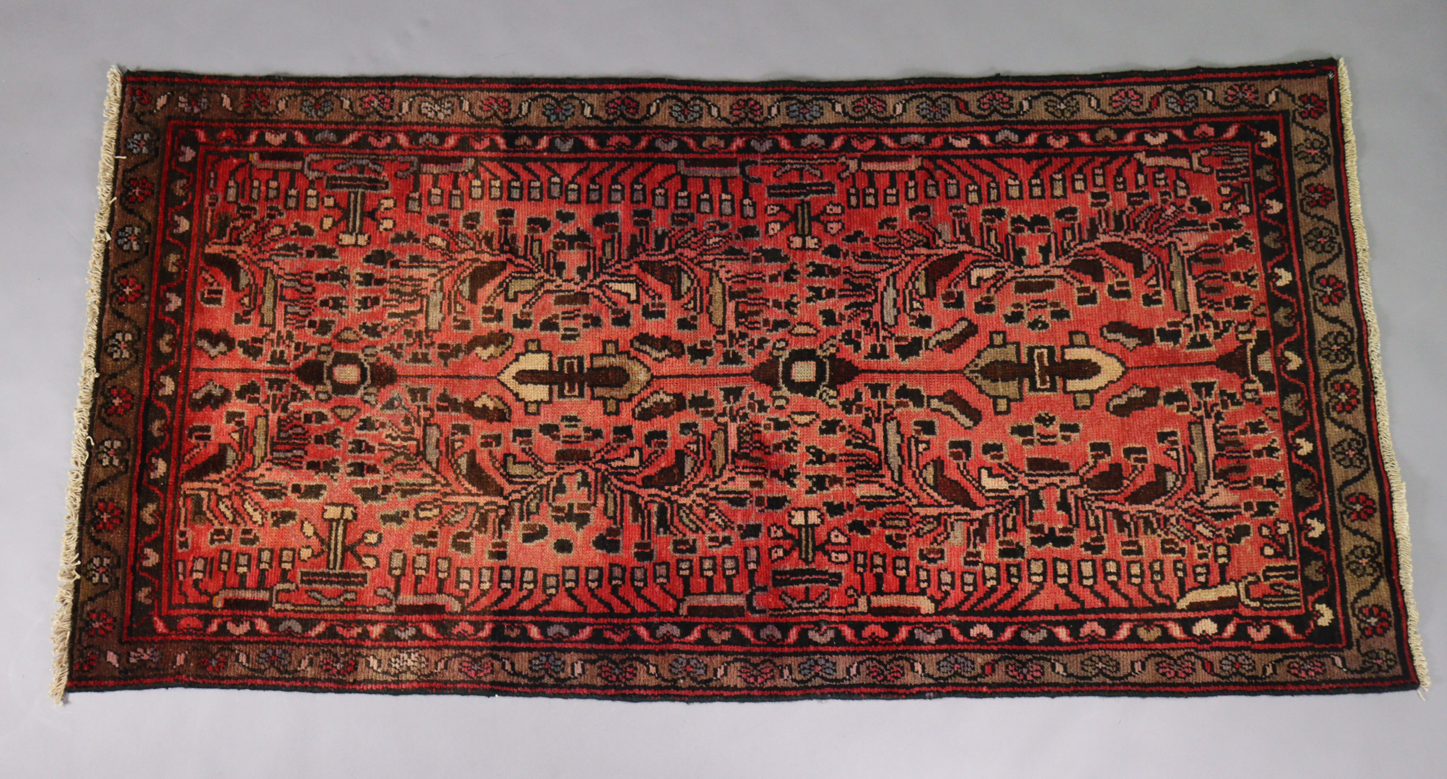 A Persian Zanjan rug of madder ground with repeating geometric designs surrounded by a wide