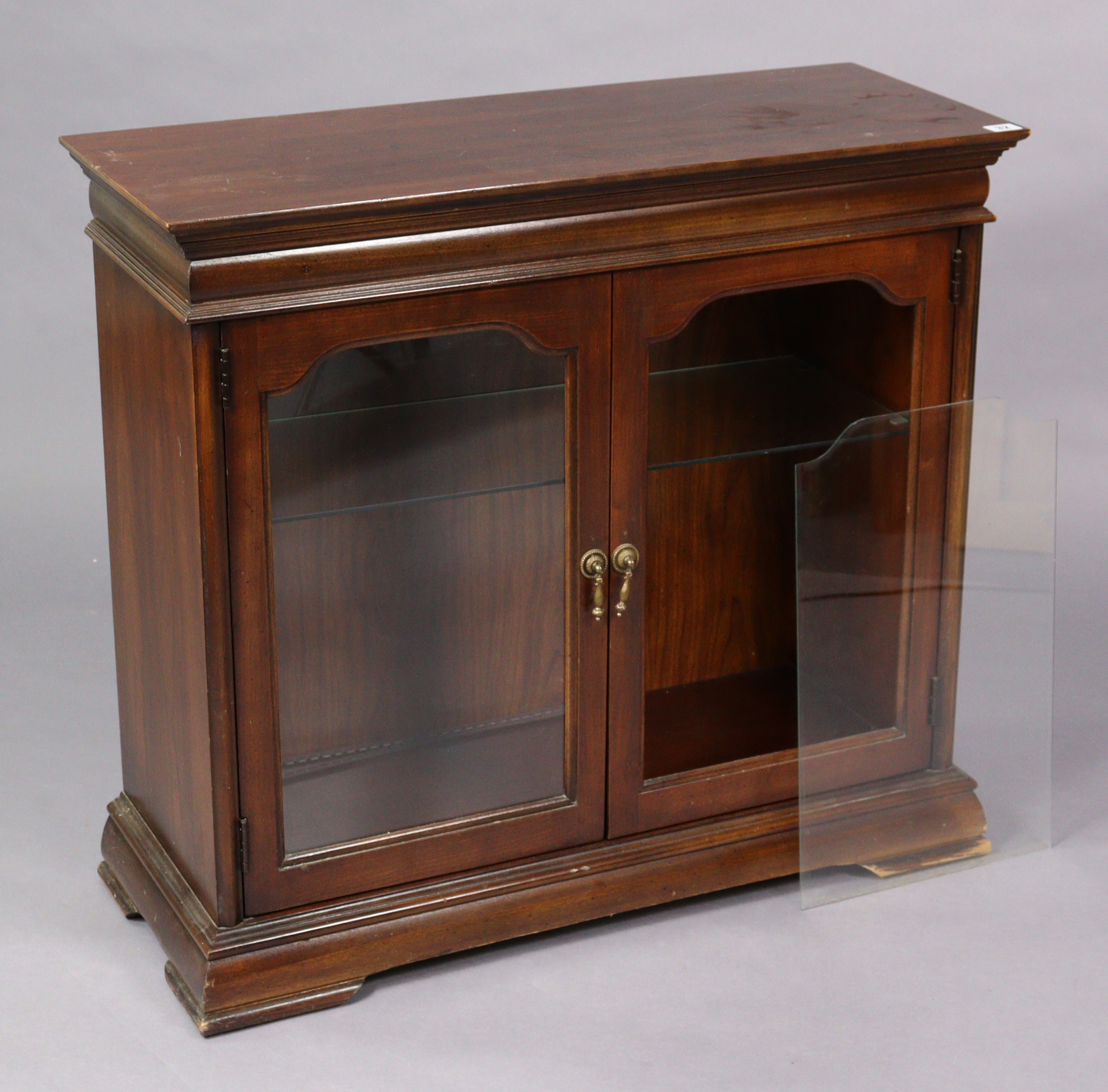 A mahogany dwarf cabinet fitted with a plate-glass shelf, & on a shaped plinth base, 33” wide x