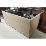 A modern fabric covered coffee table with a tinted inset glass top, on casters  16"h  35"sq