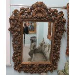 A modern ornate mirror, the bevelled plate set in a gilded hardwood frame with mask motifs and swags