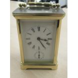 An early 20thC lacquered brass cased carriage timepiece with bevelled glass panels; faced by a Roman