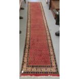 A Persian runner, decorated with repeating stylised designs, on a red ground  29" x 152"