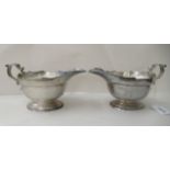 A pair of silver sauce boats, each with a cut, flared rim and a double C-scrolled handle, on a