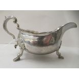 A silver sauce boat with a cut, flared rim and a double C-scrolled handle, on shell cast, pad