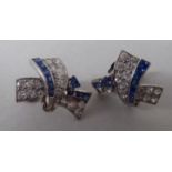 A pair of Art Deco white metal ribbon tied, sapphire and diamond set earrings