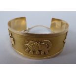 A yellow metal open bangle, decorated with three symbols, on a safety chain  stamped AG US 08