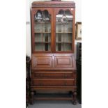 A 1930s oak bureau bookcase, having a blindfret carved frieze, over two astragal glazed doors and