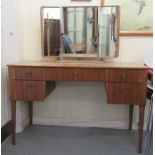 A Gordon Russell teak finished five drawer, kneehole dressing table with knob handles, surmounted by