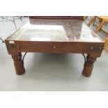 A modern Asian teak coffee table, the plate glass top over a relief carved surface, raised on turned