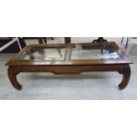 A modern Chinese inspired mahogany coffee table with two inset glass panels, raised on splayed legs