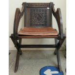 An early 20thC oak framed Glastonbury chair, carved with trailing flora, berries and stylised