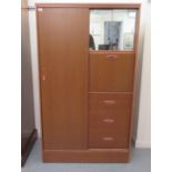 A modern teak finished compactum with an arrangement of sliding doors, a fall flap and drawers, on a