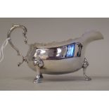 A silver sauce boat with a cut, flared rim and double C-scrolled handle, elevated on pad feet
