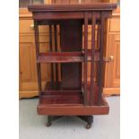 A mid 20thC mahogany revolving bookcase with two tiers and part slatted sides, raised on a crossover