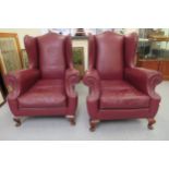 A pair of 20thC Georgian style high wingback armchairs, stud upholstered in maroon hide with cushion