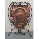 An early 20thC Arts Movement wrought iron framed firescreen, set with a shield shaped embossed