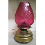 An early 20thC oil lamp, the cranberry coloured glass shade, clear glass funnel, over a brass,