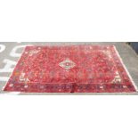 A Persian rug, decorated with stylised designs on a red ground  60" x 98"