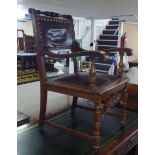 A 1930s oak framed Old English style elbow chair, the stud upholstered brown faux hide panelled back