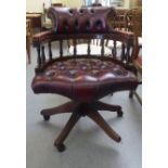 A modern mahogany finished swivel desk chair, upholstered in a faux red hide, on casters