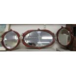 An early 20thC mahogany backed hanging triptych mirror, the bevelled oval plates set in wavy edged
